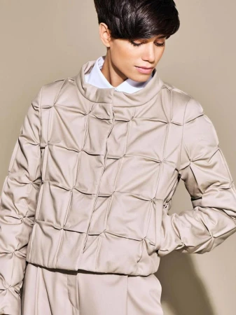 Model with short dark hair wearing a quilted beige jacket and white collared shirt against a neutral background