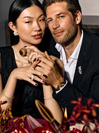 Elegant portrait of an Asian woman and Caucasian man in formal attire, posing intimately with jewelry, against a dark, romantic backdrop.
