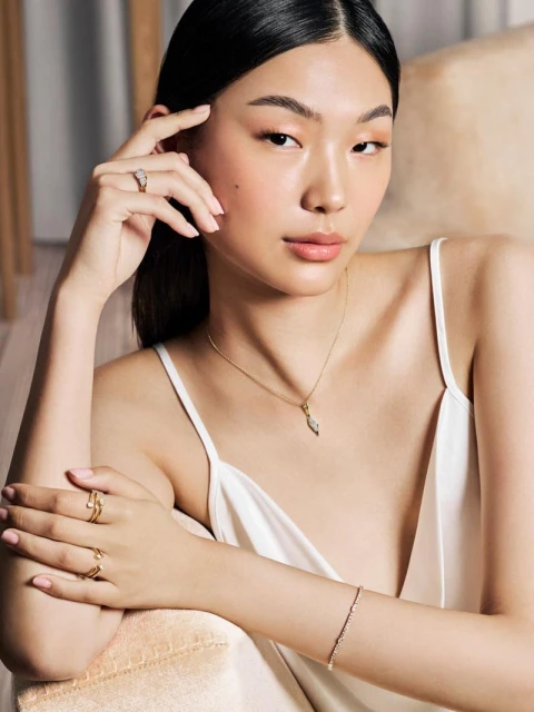Portrait of an East Asian woman wearing a white dress and gold jewelry, sitting indoors with neutral background, lit with soft light.