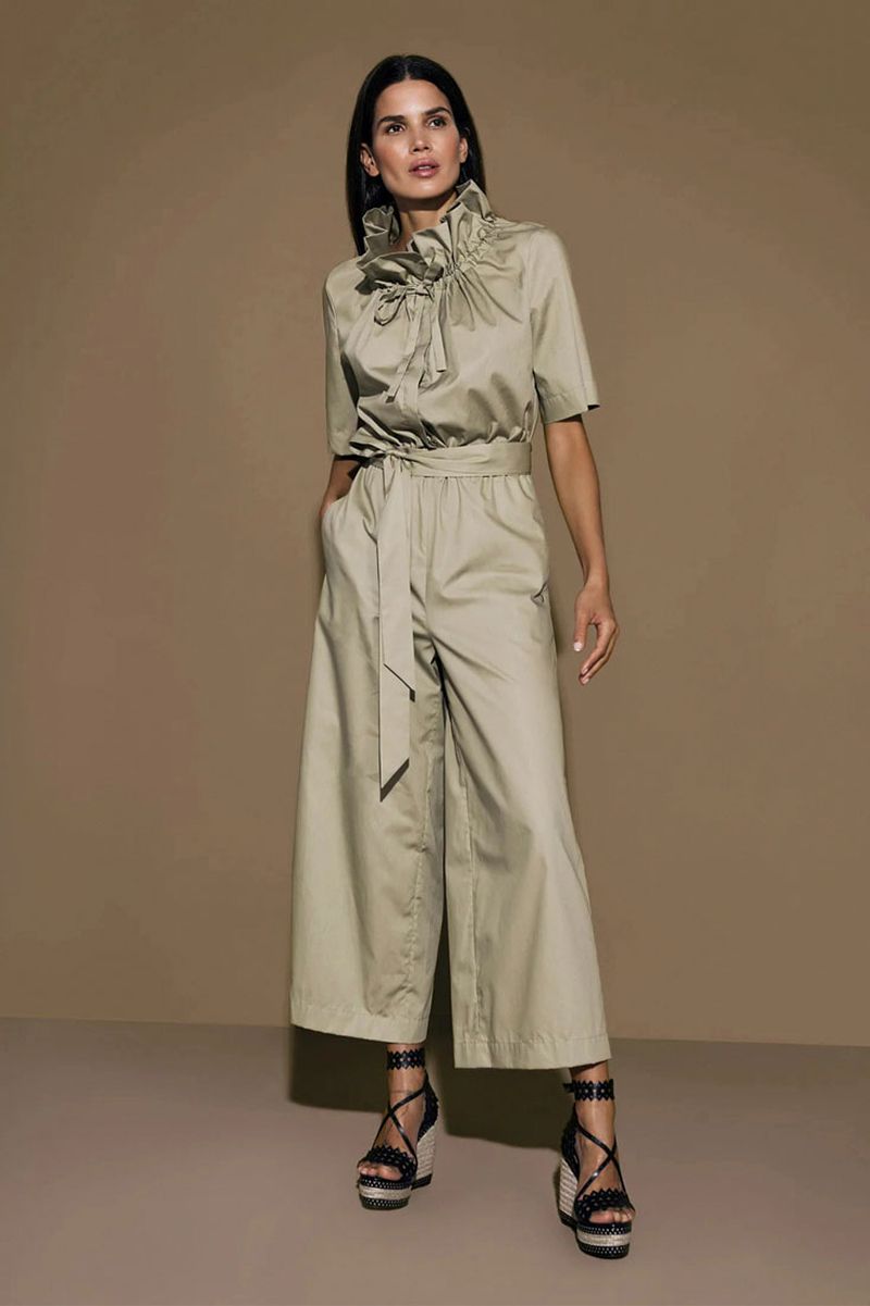 A full-length shot showcases a woman in a khaki jumpsuit, posing in a photo studio with a solid background, radiating fashion and style.