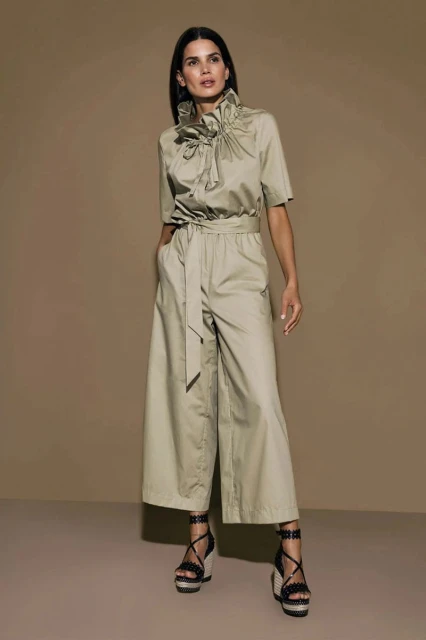 A full-length shot showcases a woman in a khaki jumpsuit, posing in a photo studio with a solid background, radiating fashion and style.