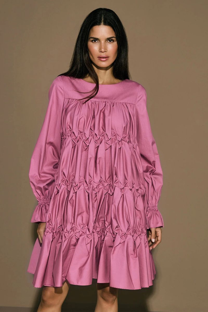Model Raica Oliveira wearing a pink smocked dress against a solid neutral background for the Armargentum Campaign photographed by Olga Rubio Dalmau.