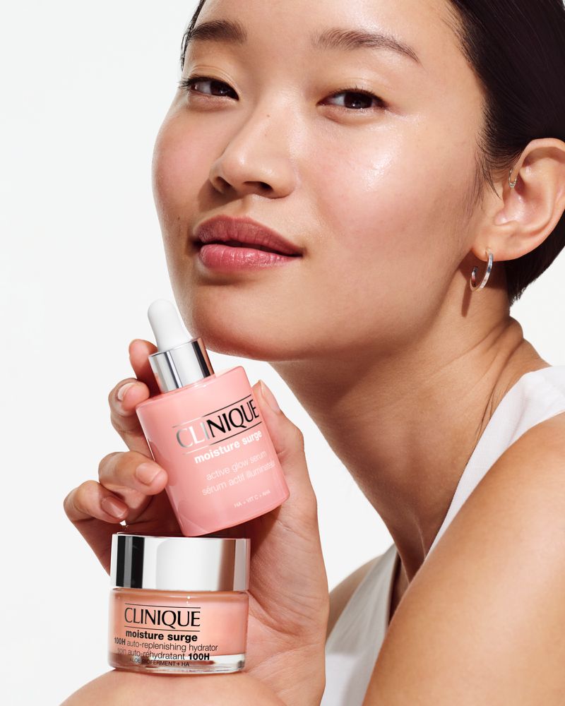 An Asian woman presents two pink-toned Clinique skincare products, emphasizing moisturization. Clean beauty aesthetic.