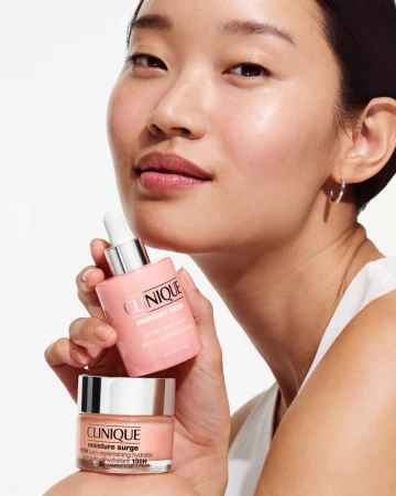 An Asian woman presents two pink-toned Clinique skincare products, emphasizing moisturization. Clean beauty aesthetic.
