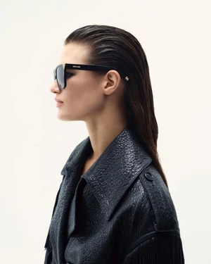 Profile portrait of a female model wearing black sunglasses and a textured black leather coat against a white background.