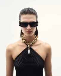 Model wearing black sunglasses and a chunky gold chain necklace against a white background for Roberto Cavalli