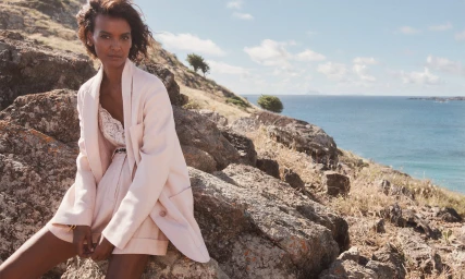 Liya Kebede seated on rocky terrain overlooking the ocean, wearing a light pink blazer and matching shorts by Zimmermann.