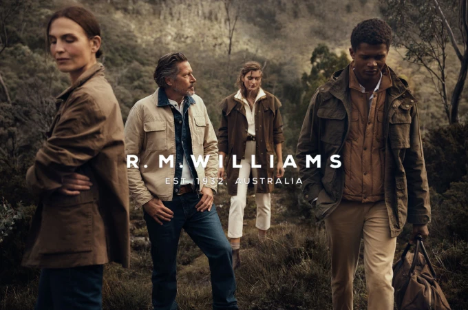 Four people in outdoor apparel stand in a field with trees in the background, showcasing the R.M. Williams brand and its Australian roots.
