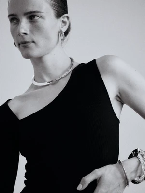 Model wearing silver necklace and bracelets in a black top against a plain light background