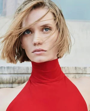 Close-up portrait of a woman with blonde hair wearing a bright red turtleneck top against a neutral background.