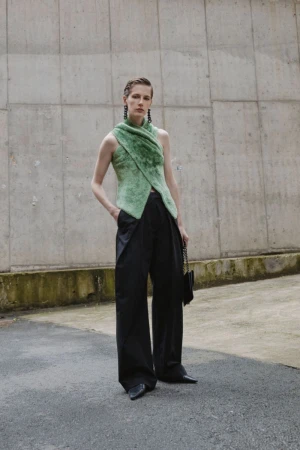 Model wearing a green textured top and black trousers standing against a concrete wall for Christian Wijnants AW 2024.