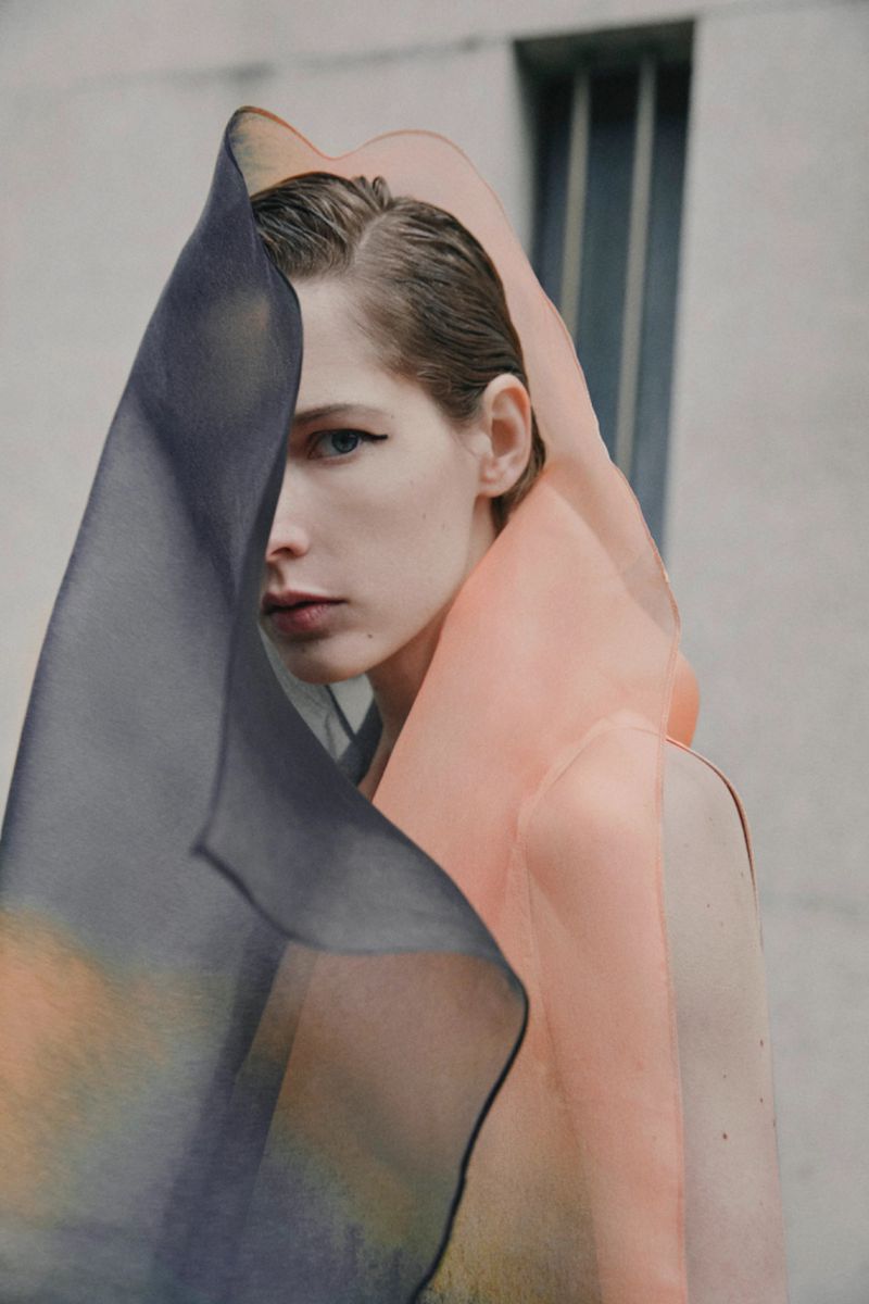Close-up portrait of a fair-skinned adult woman wearing a sheer, peach-colored garment that is partially obscured by a sheer, blue fabric.