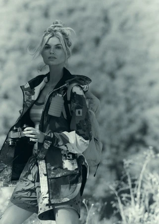 Blonde woman wearing outdoor apparel and carrying a backpack holding binoculars outdoors in a natural landscape setting