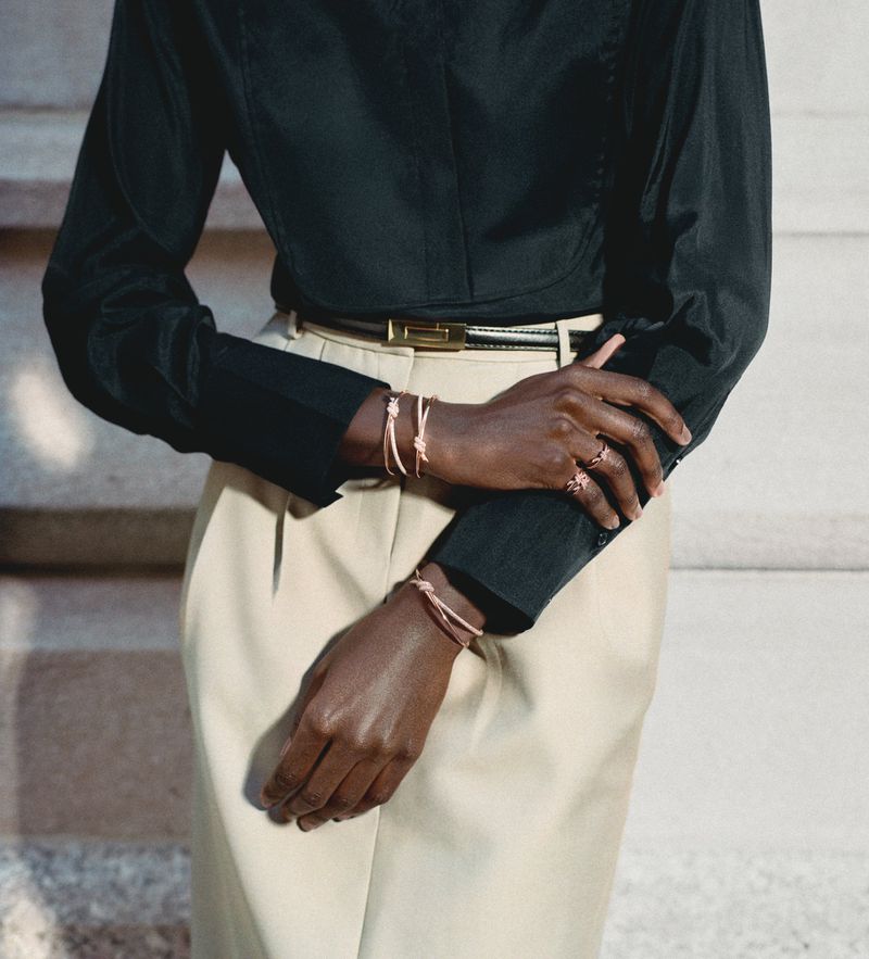 Mid-section studio shot featuring a dark-skinned adult female model wearing bracelet jewelry, a black long-sleeve top, and tan skirt.