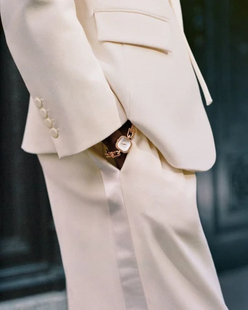 Close-up of a stylish cream-colored suit with a square-faced gold watch accentuating the wrist, set against a neutral backdrop.