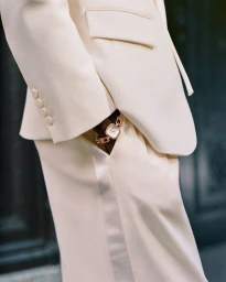 Close-up of a person wearing a cream suit and a gold link watch with hand in pocket