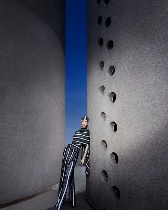 Model in a black and white striped dress leaning against a large industrial textured concrete structure