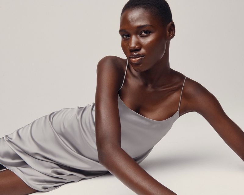 Elegant woman in a slip dress poses in front of a neutral backdrop, showcasing minimalist fashion and clean studio lighting.