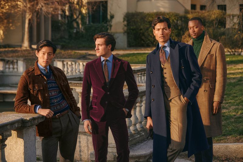 Four diverse male fashion models pose outdoors in tailored suits and overcoats, showcasing a range of earth-tone colors and fabrics.