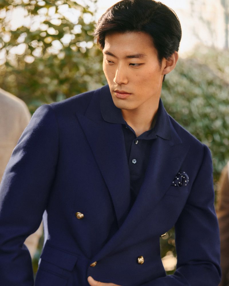 Portrait of an Asian man wearing a blue double-breasted blazer and collared shirt posing outdoors in soft, diffused light.