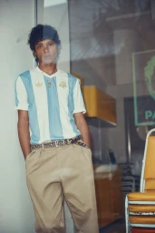 Model wearing a blue and white striped jersey and khaki trousers leaning against a wall for Simons Canada