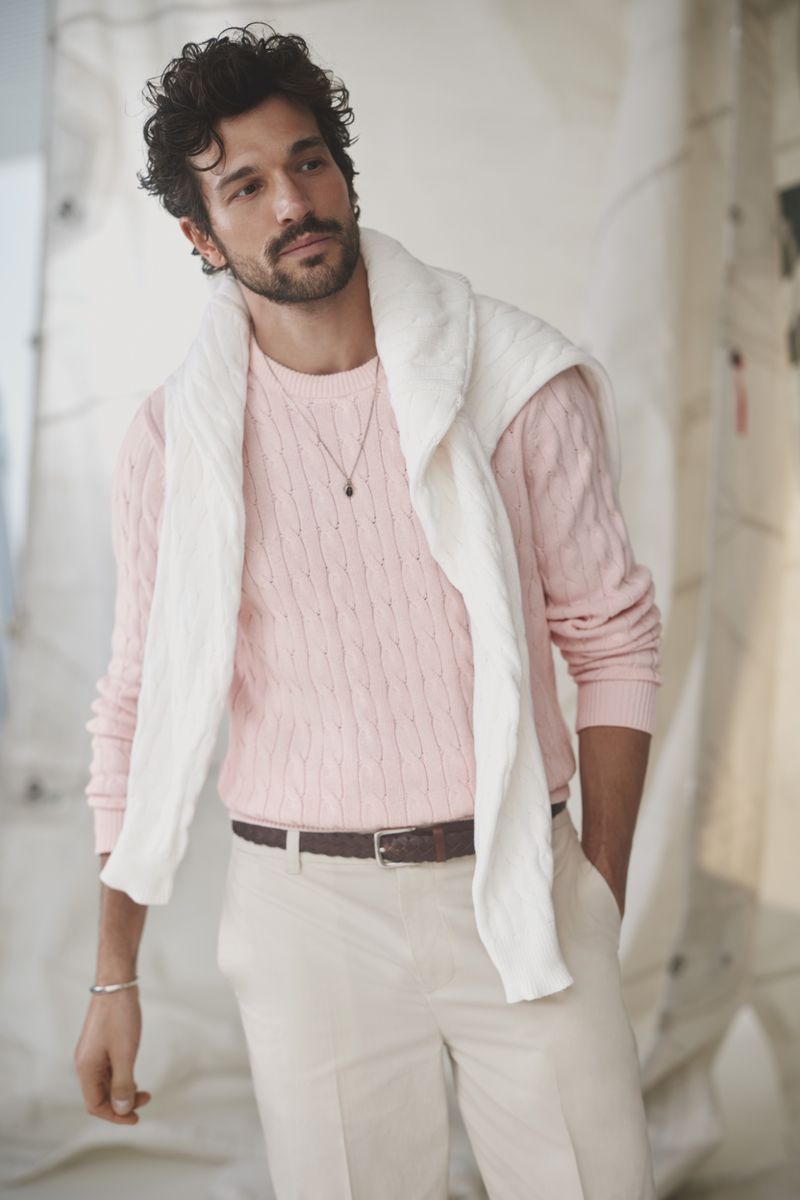 Model wearing a pink cable knit sweater with a white sweater draped over his shoulders for Simons Canada