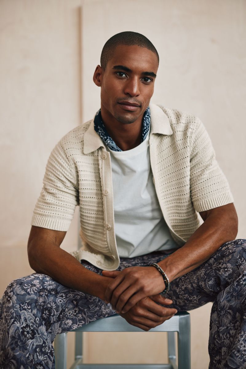 Model Malik Lindo wearing a cream knit polo shirt and patterned trousers for Simons Canada
