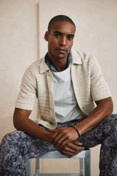 Model Malik Lindo wearing a cream knit polo shirt and patterned trousers for Simons Canada