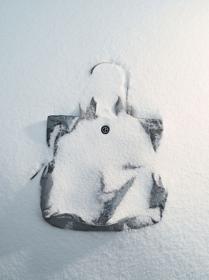 Fashionable grey tote bag dusted with snow on white backdrop, creating a minimalistic winter fashion statement in a cool aesthetic.
