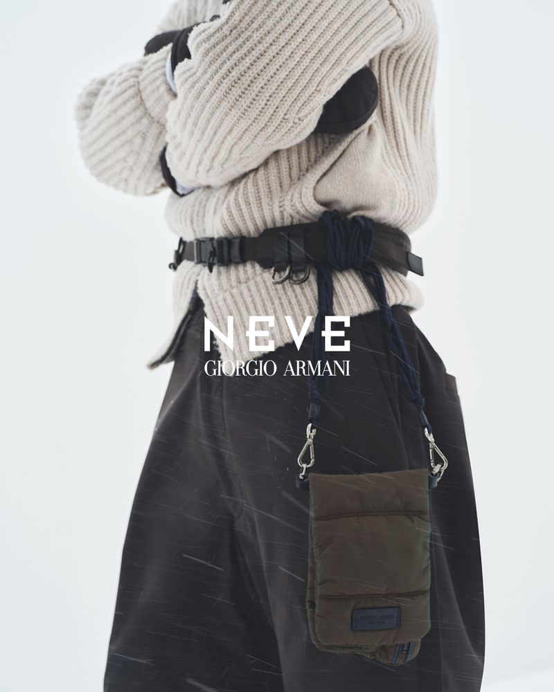 Close-up of a person in winter clothing with a textured sweater, dark trousers, and a small olive green bag in a snowy environment.