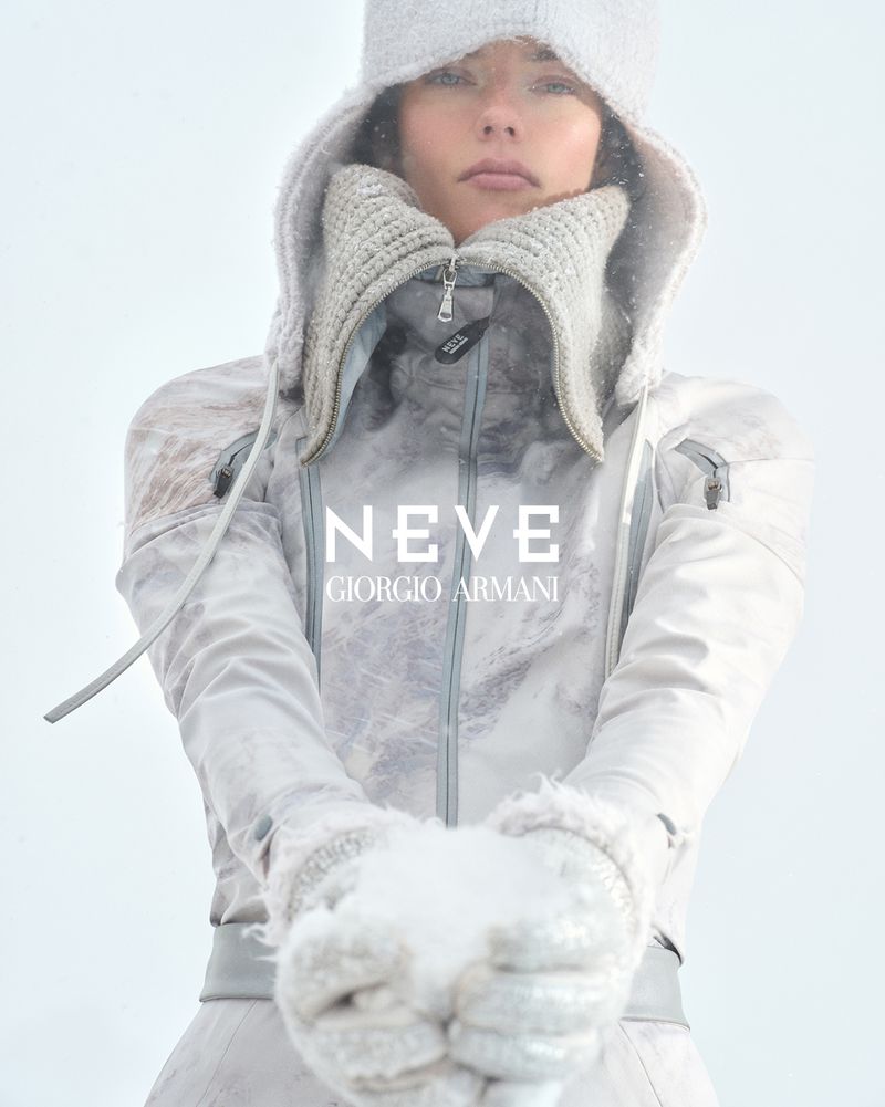 Fashion shot of a woman in winter outerwear and snow gloves, holding snow in her gloved hands, with a cool and muted color palette.