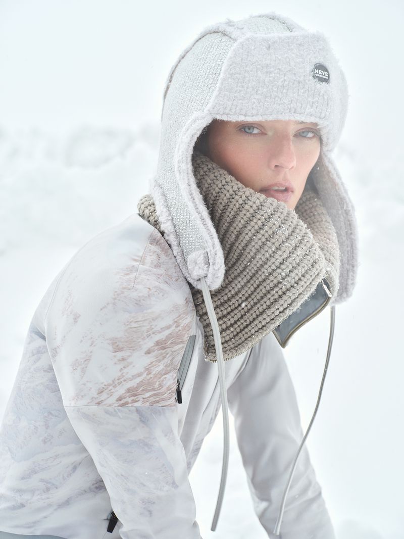 Portrait of a woman in winter clothing, featuring a knit hat and scarf, set against a blurred, snowy outdoor backdrop in soft lighting.