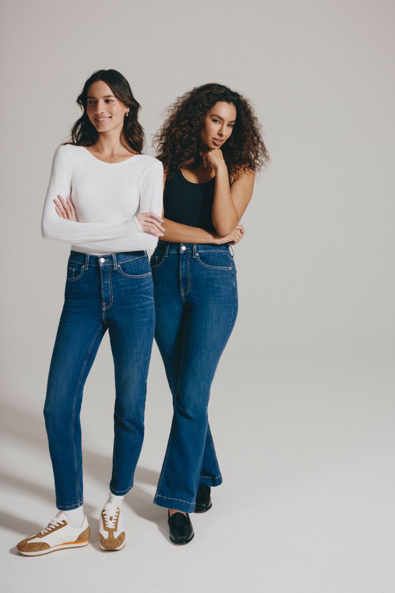 Two women posing in denim jeans and casual tops against a seamless white studio background