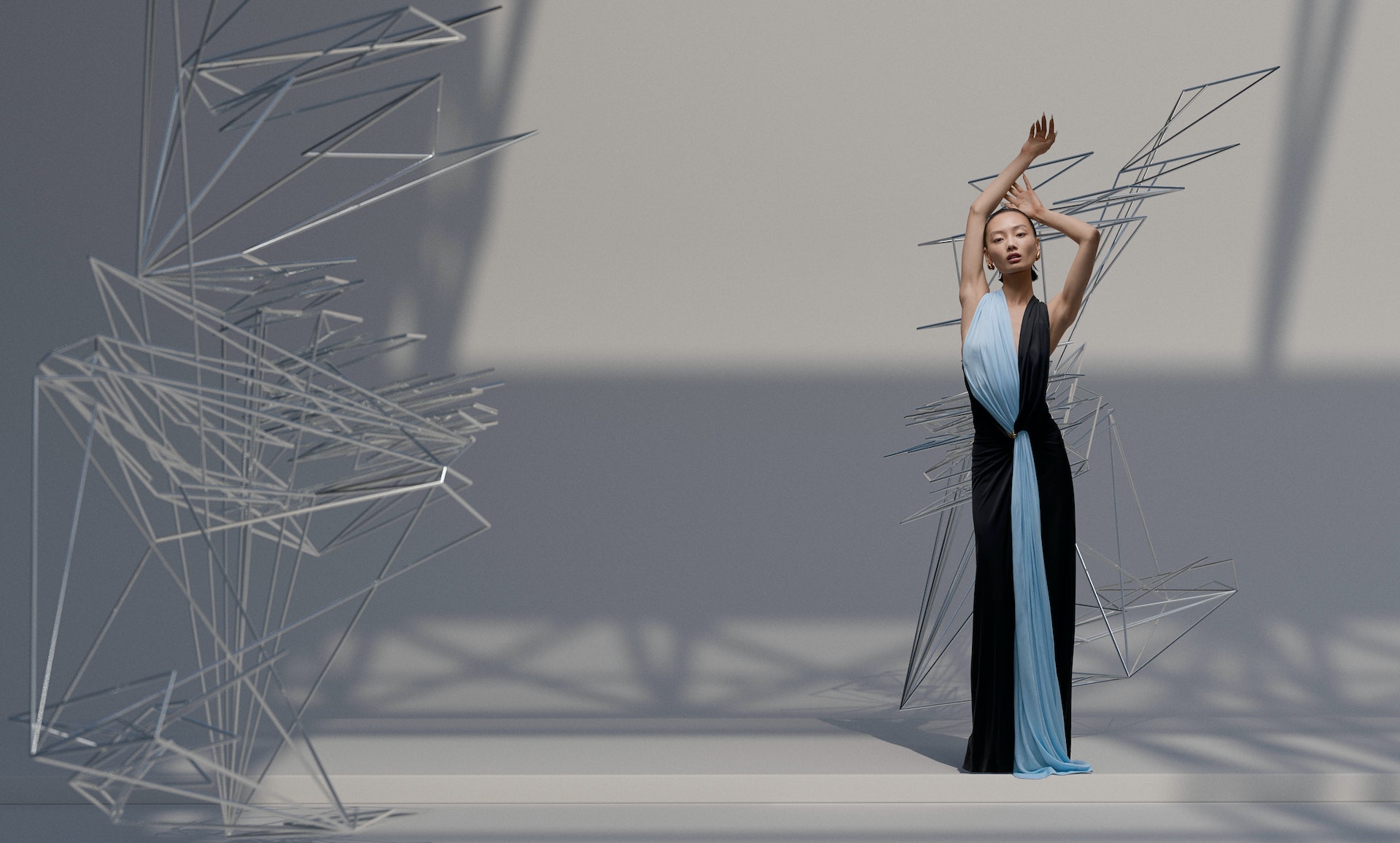 An Asian woman poses in a striking blue-and-black gown, gracefully framed by abstract geometric sculptures in a minimalist studio setting.