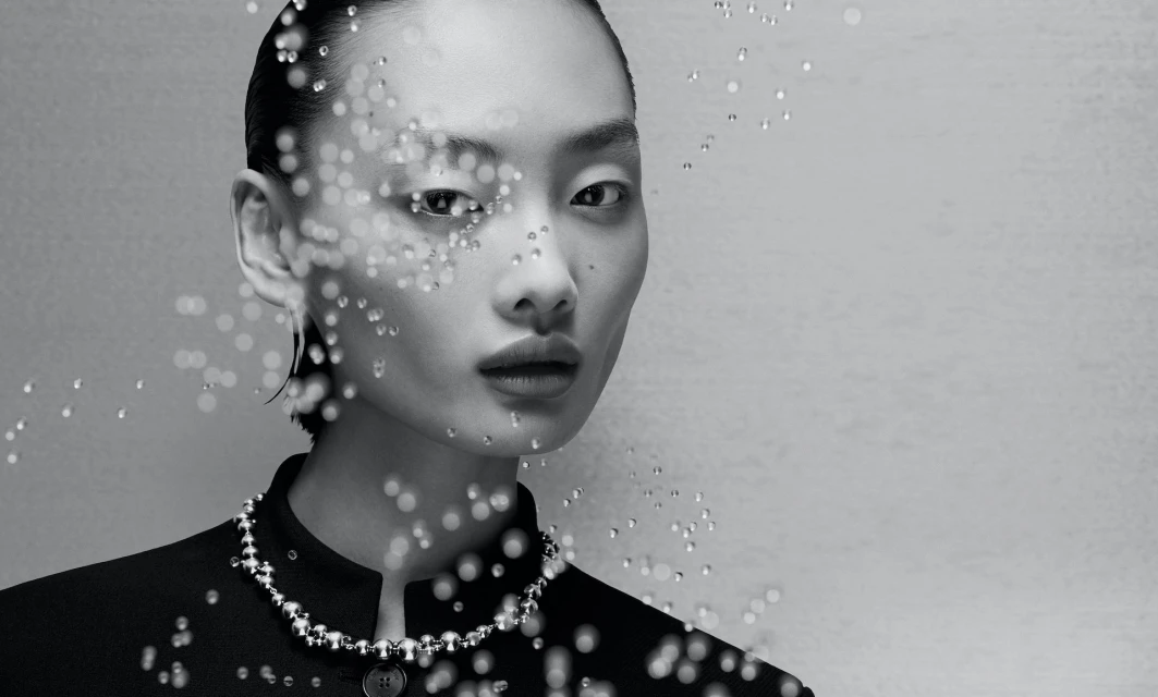 Monochrome portrait of an Asian woman with water droplets, wearing a black collared shirt and necklace against a light gray background.