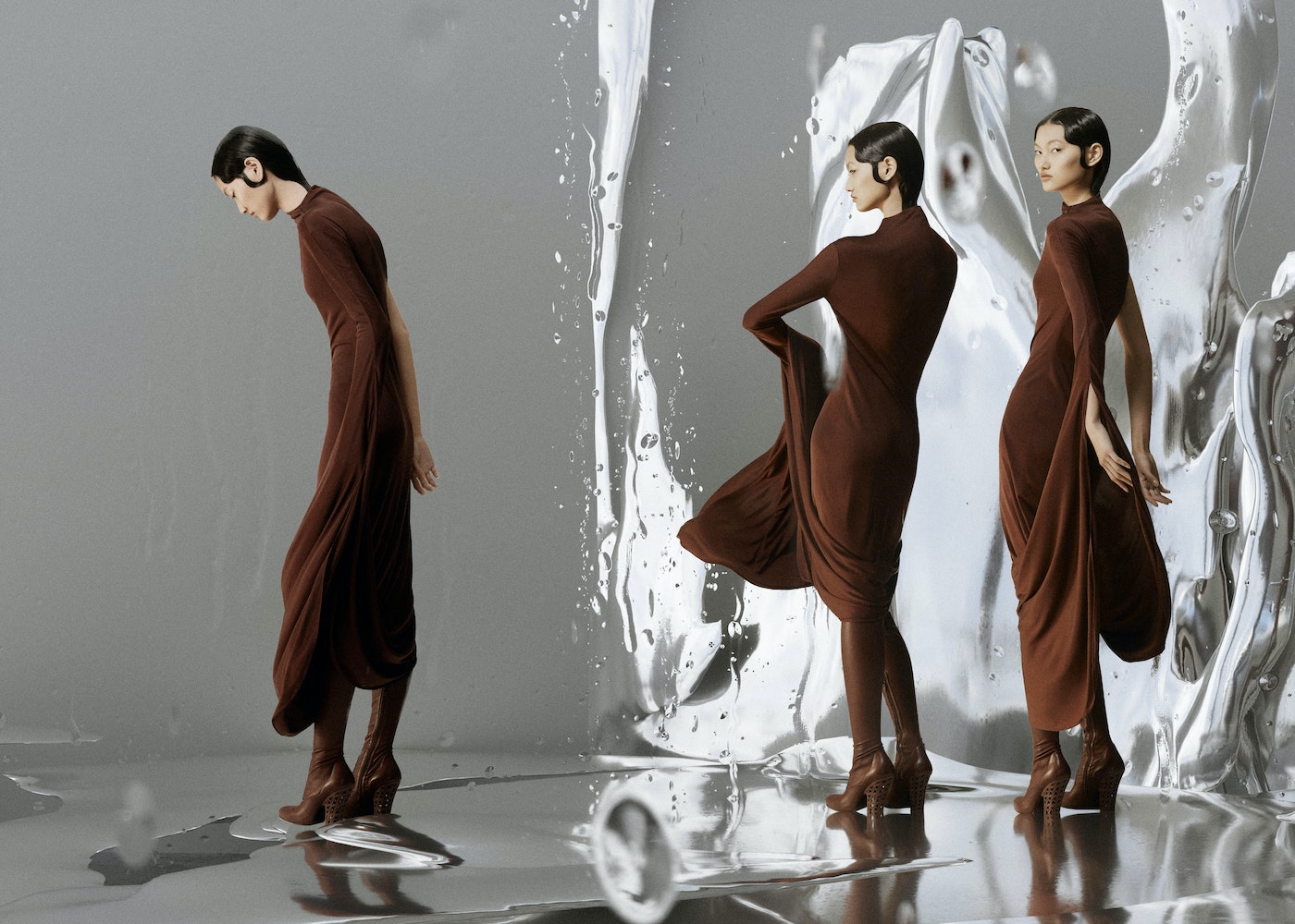 Three women pose in brown dresses with sculptural silver backdrop. Fashion shoot with reflective surface and elegant, contemporary design.
