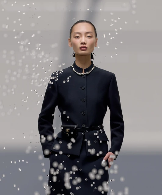 Elegant Asian woman in a navy suit and pearls, adorned with glistening water droplets in a fashion shot with a grey gradient background.