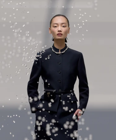 Elegant Asian woman in a navy suit and pearls, adorned with glistening water droplets in a fashion shot with a grey gradient background.