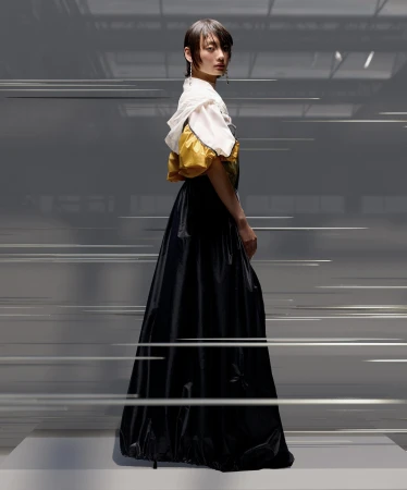 Model in a black skirt and white and yellow top standing against a grey studio background with motion blur streaks