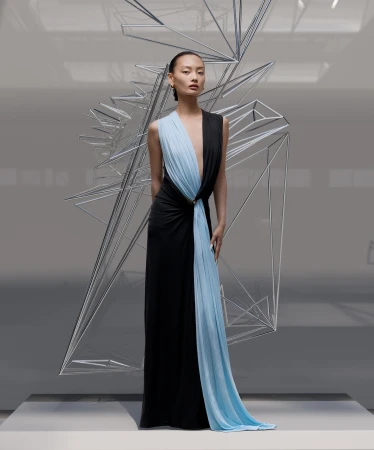 Elegant Asian woman poses in a striking black and blue gown next to modern geometric art installation in a bright, minimalist setting.