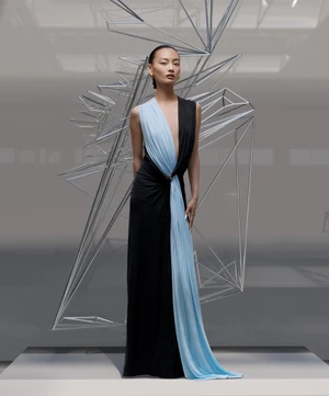Model standing in front of an abstract geometric wire sculpture wearing a black and blue evening gown.