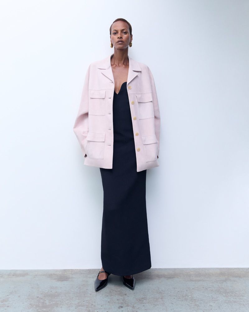 Model Yasmin Warsame wearing a pink utility jacket and black dress against a white studio background.