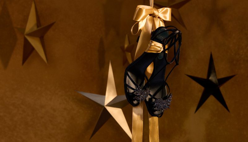 Elegant black strappy heels displayed against a gold star background with matching gold ribbon accent, showcasing luxury fashion.