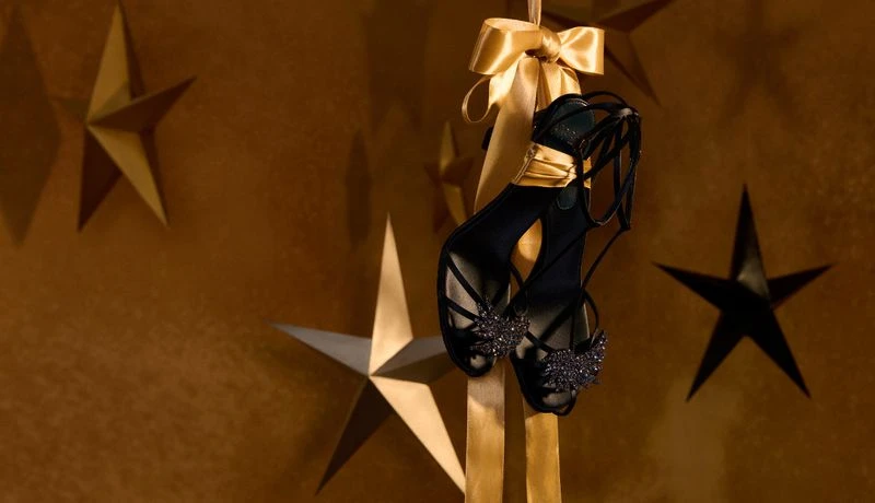 Elegant black strappy heels displayed against a gold star background with matching gold ribbon accent, showcasing luxury fashion.