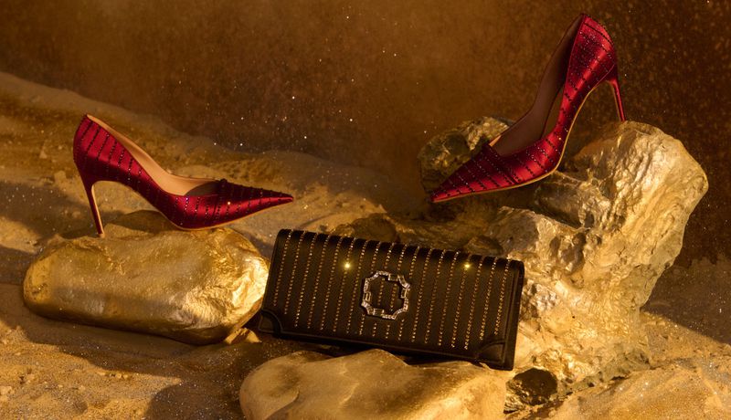 Elegant fashion still life featuring red high heels placed on rocks alongside a black clutch purse with a metallic emblem.