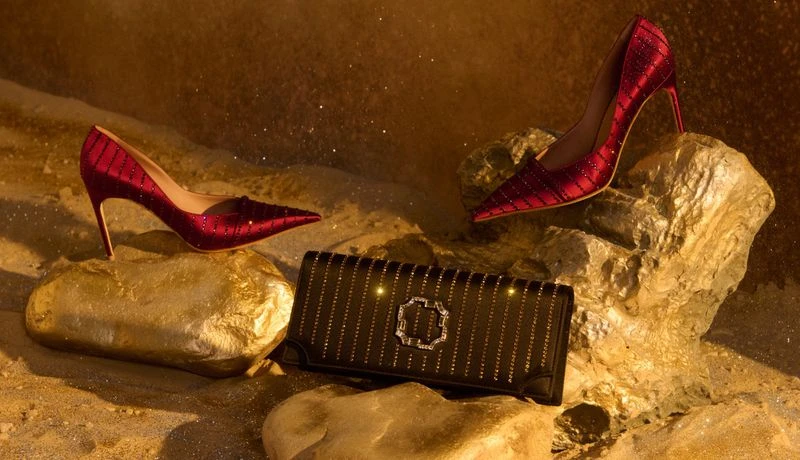 Elegant fashion still life featuring red high heels placed on rocks alongside a black clutch purse with a metallic emblem.