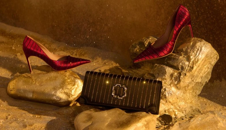 Elegant fashion still life featuring red high heels placed on rocks alongside a black clutch purse with a metallic emblem.