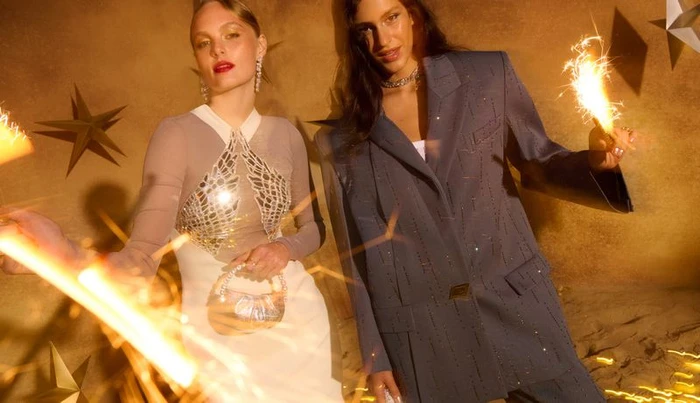 Two models holding sparklers against a warm textured wall decorated with golden star ornaments for Bloomingdale's Festive campaign
