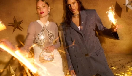 Two models holding sparklers against a warm textured wall decorated with golden star ornaments for Bloomingdale's Festive campaign