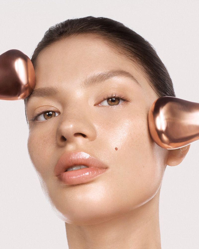 Close-up of a beautiful young woman with bronze beauty globes on her face against a clean, neutral backdrop in a studio environment.
